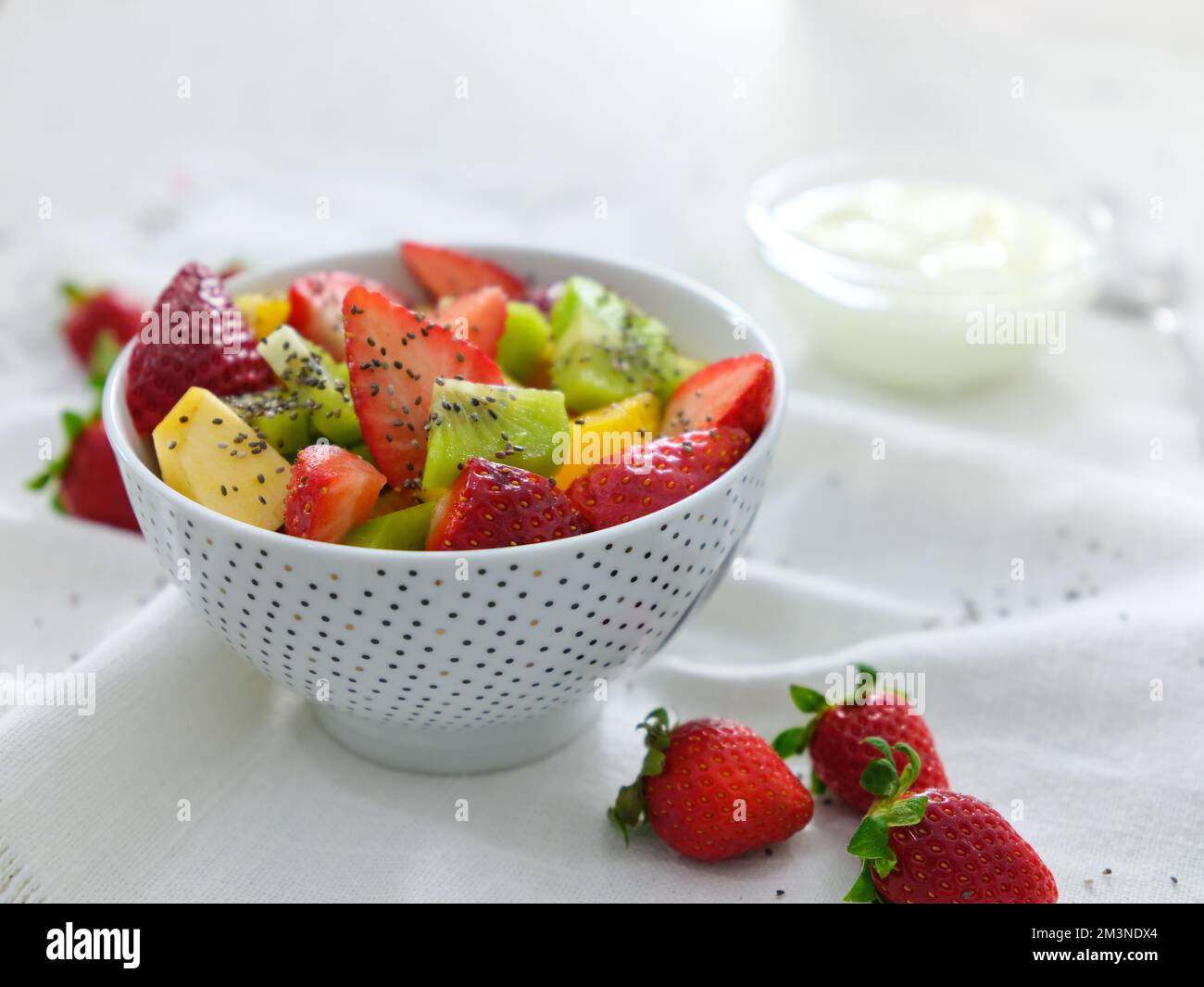 Mezcla la ensalada de frutas con yogur sobre fondo blanco. Dieta vitamínica con kiwi de fresa y naranja Foto de stock