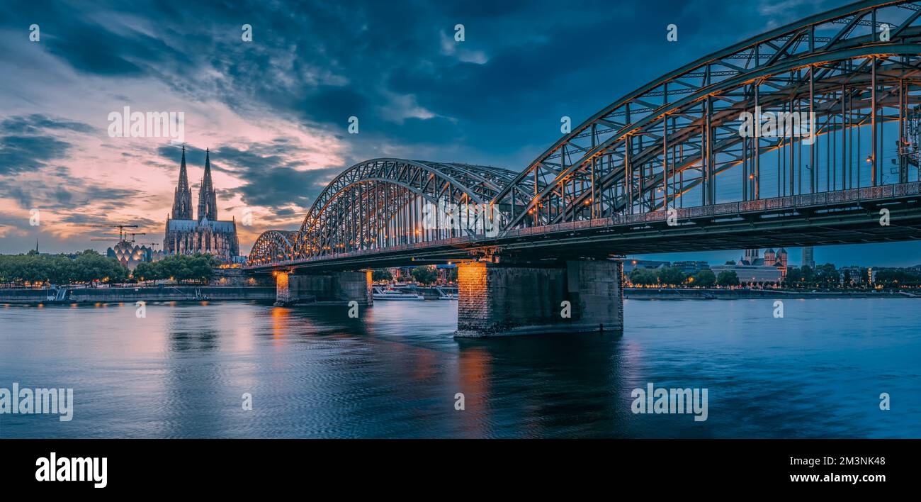 Vista panorámica del puente iluminado sobre el río Rin con trenes y  turistas que pasan y la catedral de Colonia por la noche en la hora azul  Fotografía de stock - Alamy