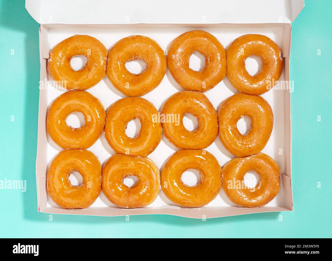 Vista aérea de donuts vidriados en una caja de entrega blanca sobre una superficie de color aqua Foto de stock