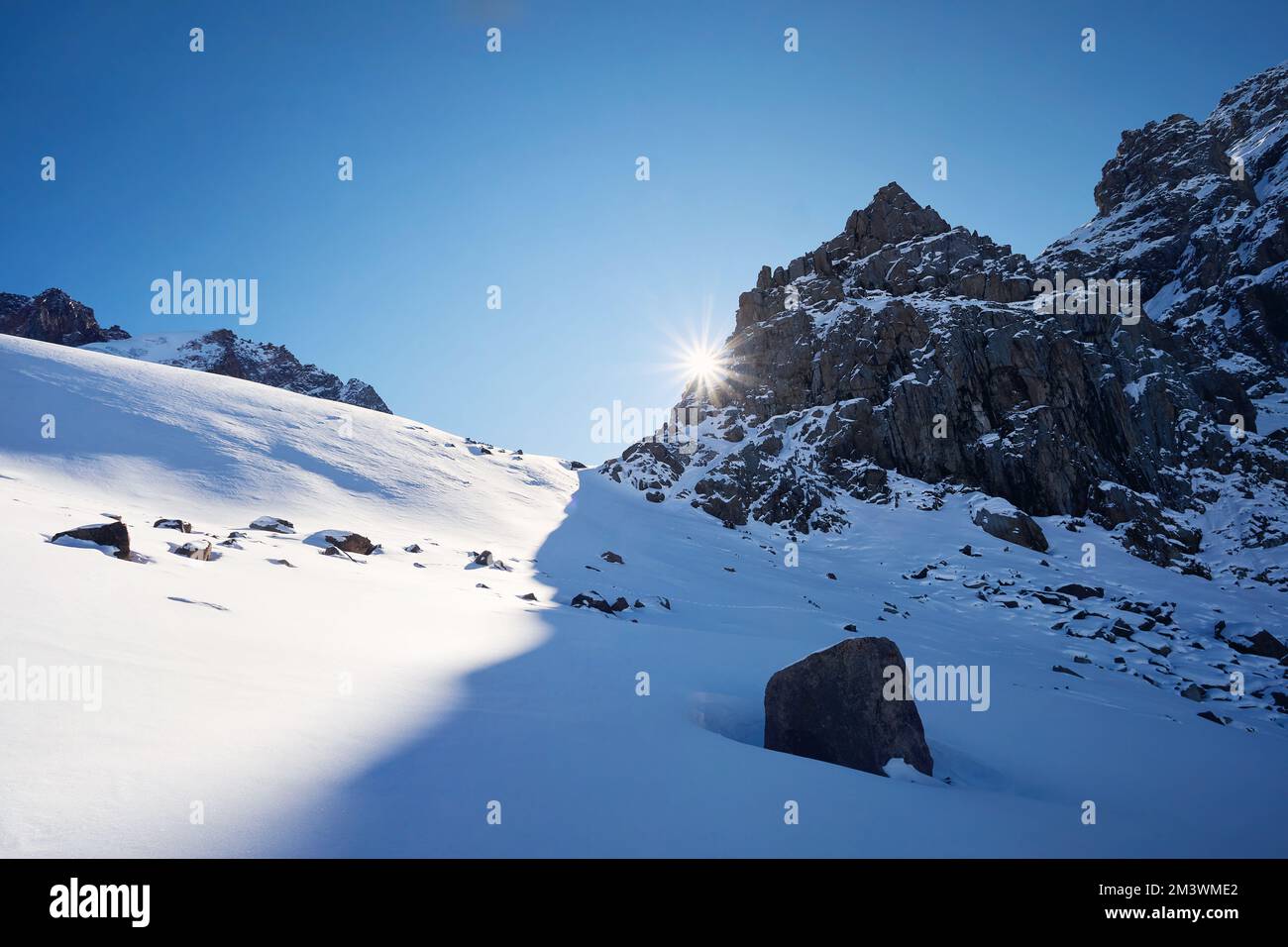 Día soleado en el paisaje de altas montañas de nieve con resplandor del sol contra el cielo azul en el tiempo de invierno en Kazajstán Foto de stock