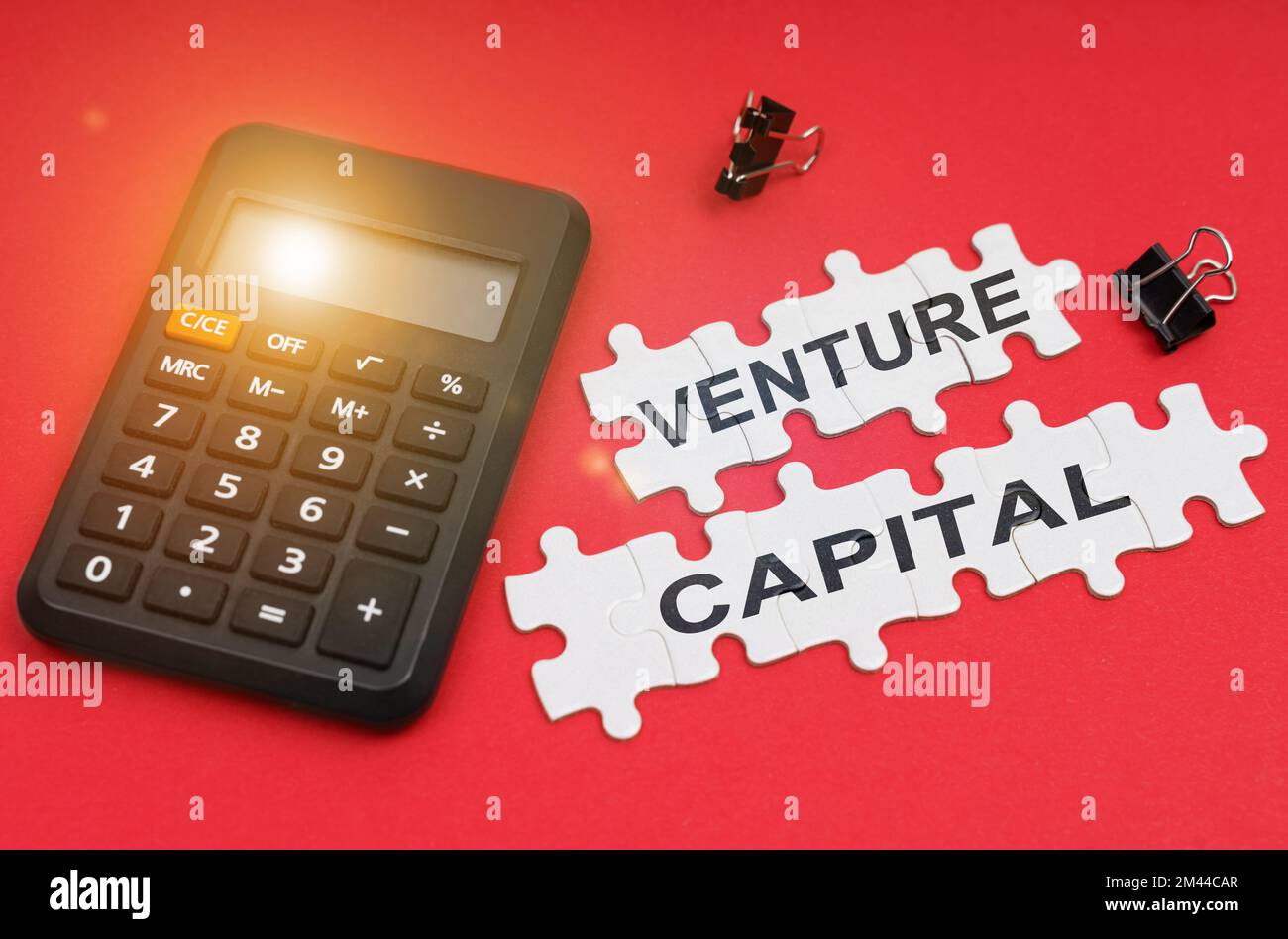 Concepto de finanzas y economía. En la superficie roja hay una calculadora, abrazaderas y rompecabezas con la inscripción - Venture capital Foto de stock
