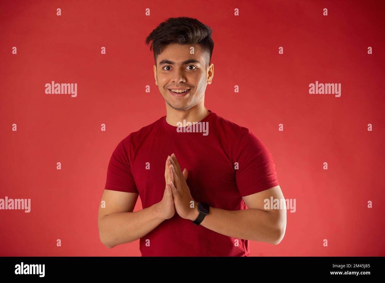 Joven saludando con gesto de namaste contra fondo rojo Foto de stock