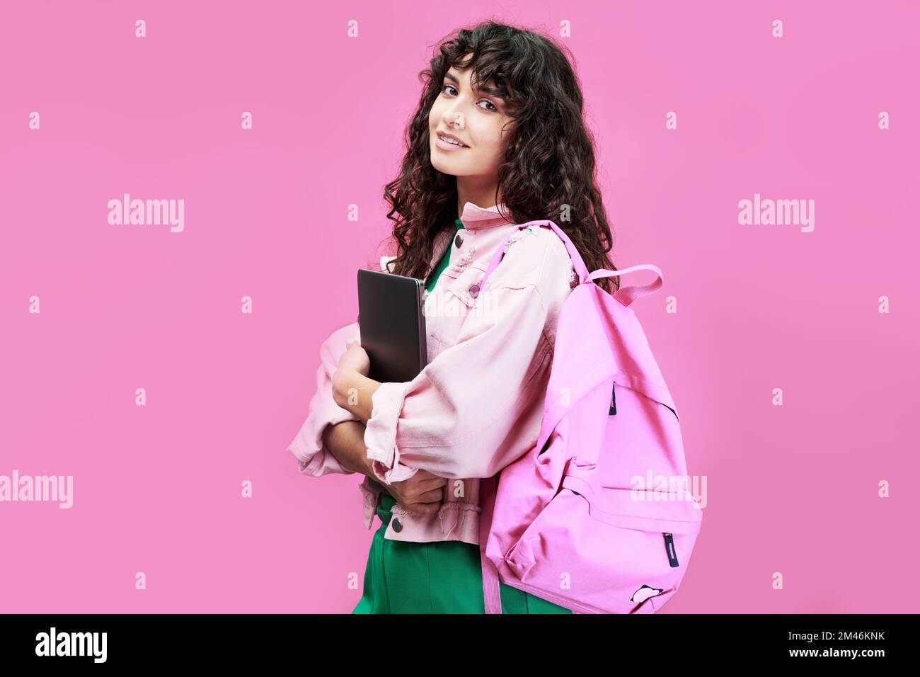 Estudiante femenina inteligente de la universidad o escuela secundaria con chaqueta de mezclilla de pie frente a la cámara contra el fondo rosa Foto de stock