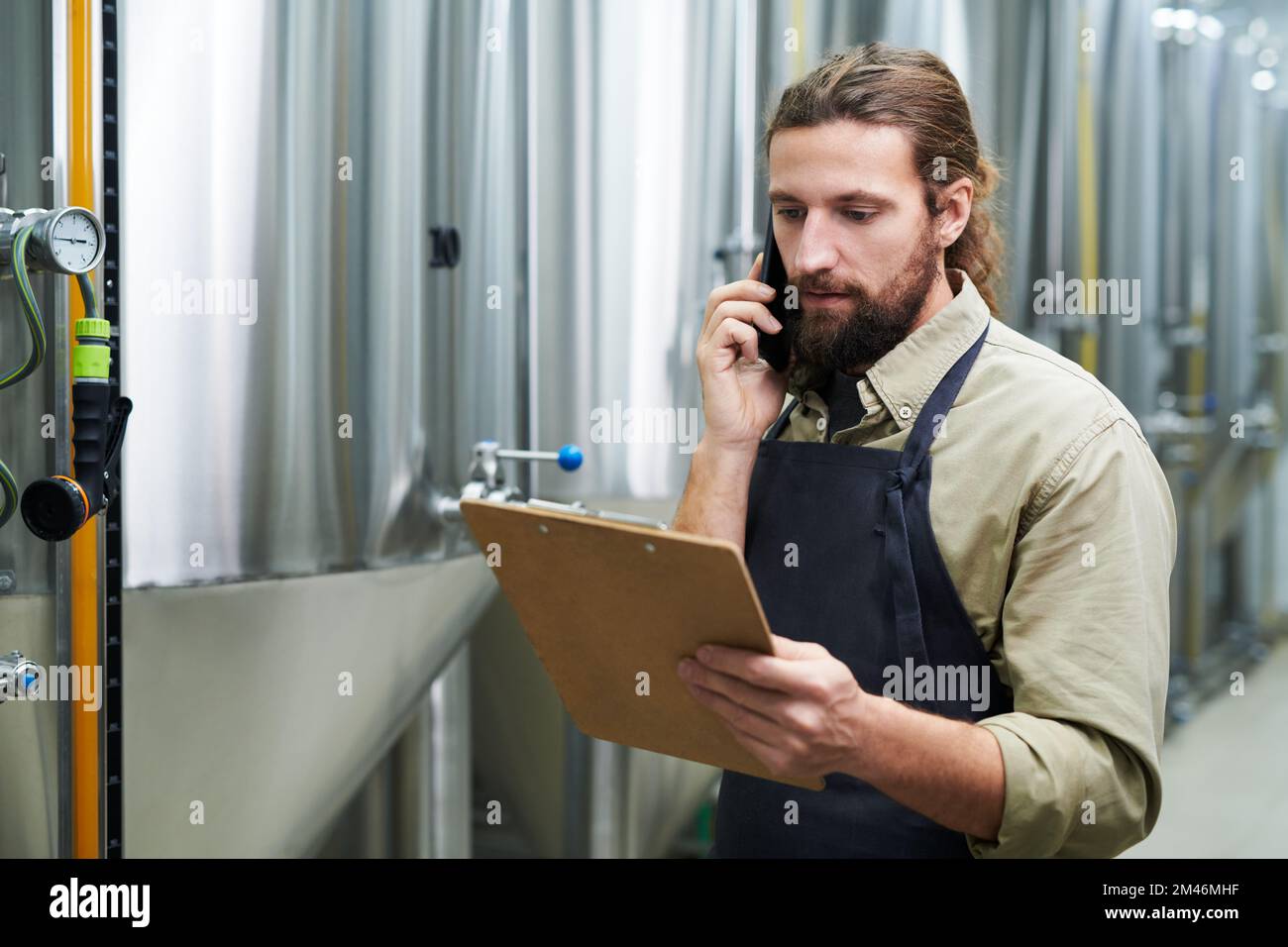 Retrato del propietario de la cervecería hablando por teléfono y pidiendo cebada malteada, lúpulo y levadura Foto de stock