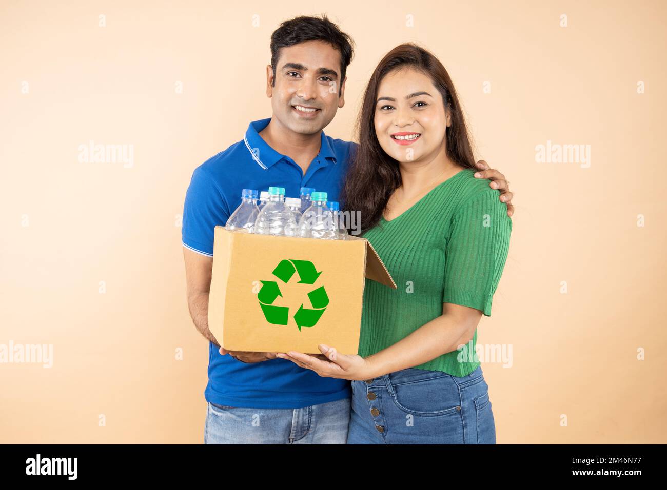 Feliz pareja india joven respetuosa del medio ambiente sosteniendo una caja llena de botellas de plástico para el reciclaje. Protección del medio ambiente, concepto del día de la tierra Foto de stock