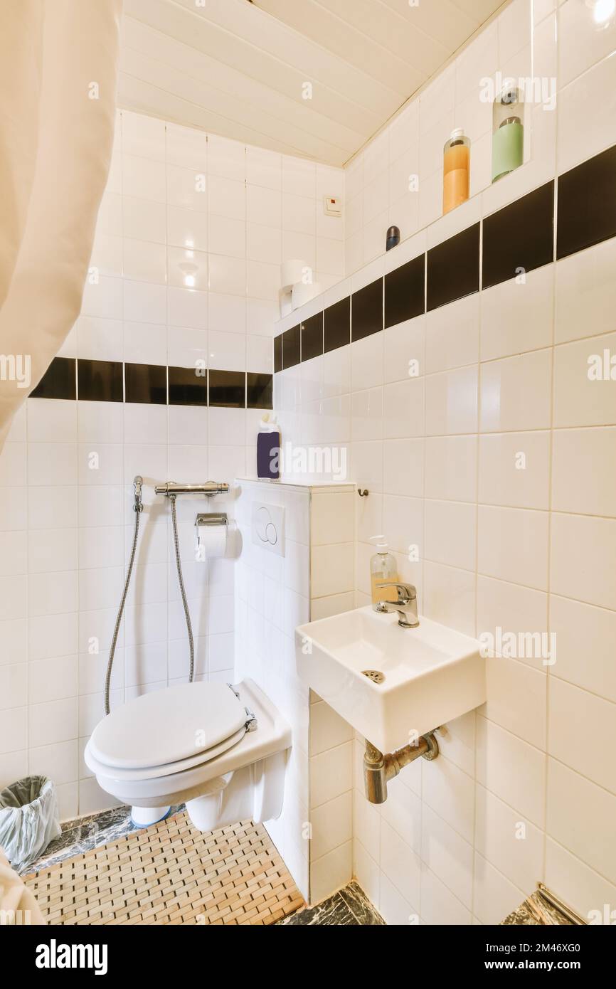 un cuarto de baño con azulejos blancos y negros en las paredes, el piso y el inodoro en su zona de esquina Foto de stock