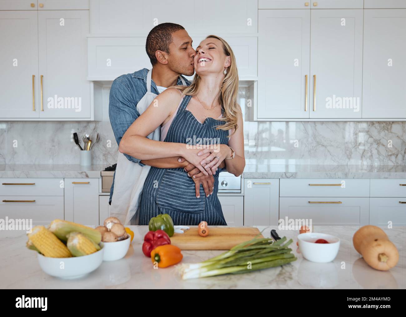Pareja, cocinando comida y amor por las verduras con un beso en la mejilla mientras ayudan con la cena en casa. Hombre y mujer en el Reino Unido con un estilo de vida saludable Foto de stock