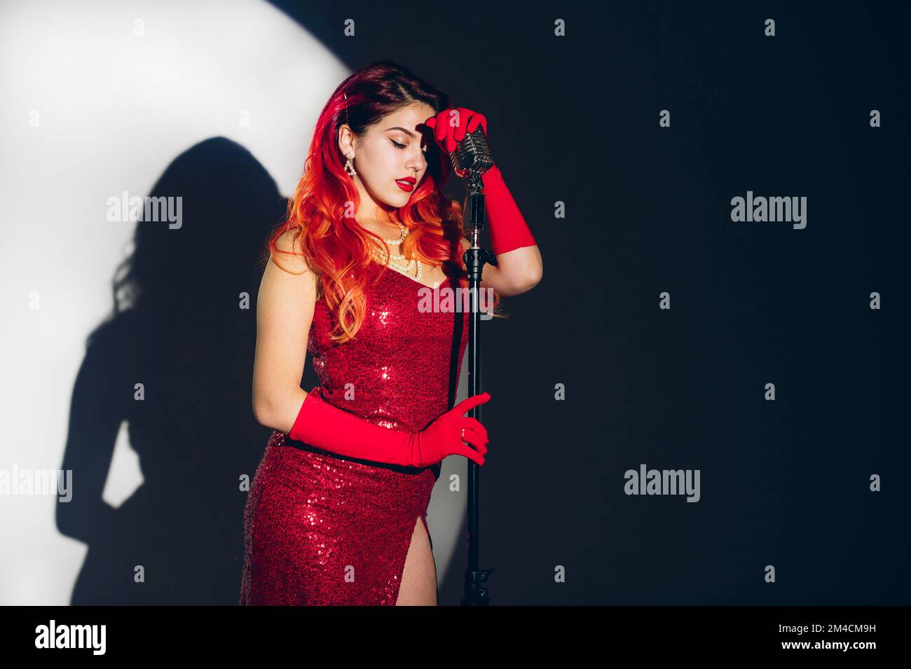 Mujer bonita en vestido rojo brillante con un pelo rojo sosteniendo micropho Foto de stock