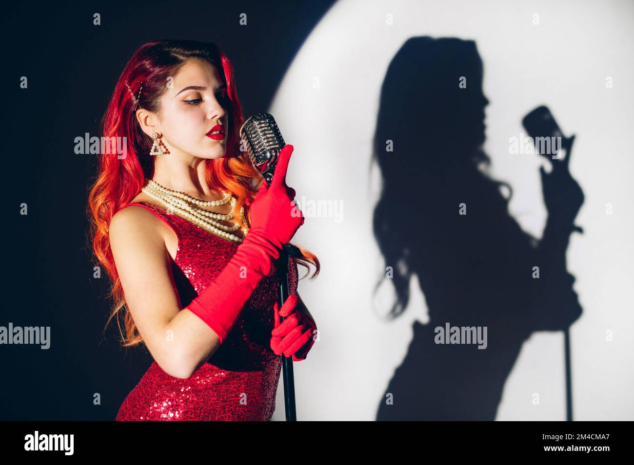 Mujer bonita en vestido rojo brillante con un pelo rojo sosteniendo micropho Foto de stock