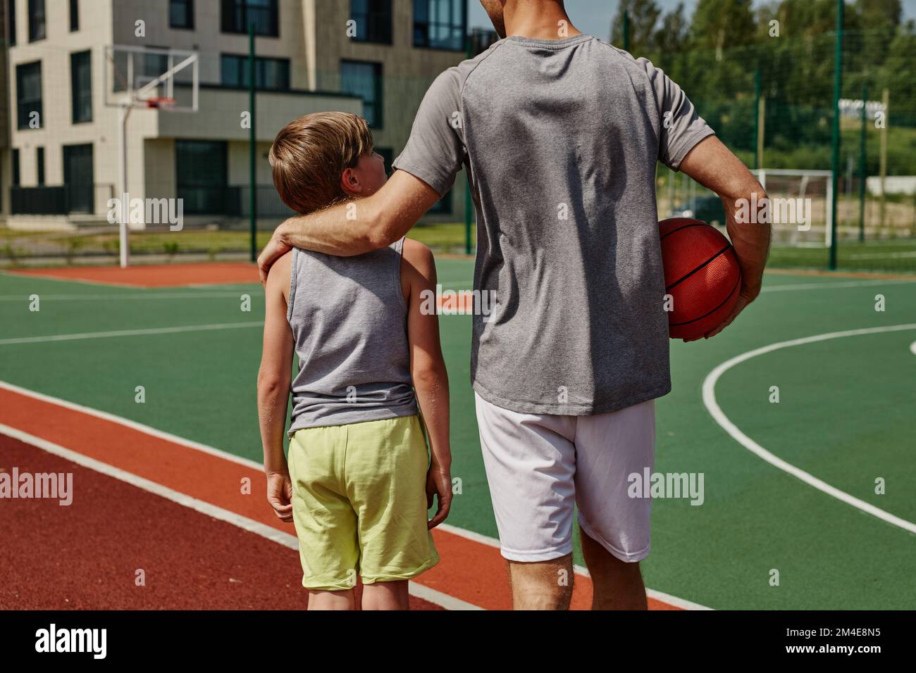 Vista trasera de padre e hijo jugando baloncesto juntos y de pie en la cancha abrazando Foto de stock