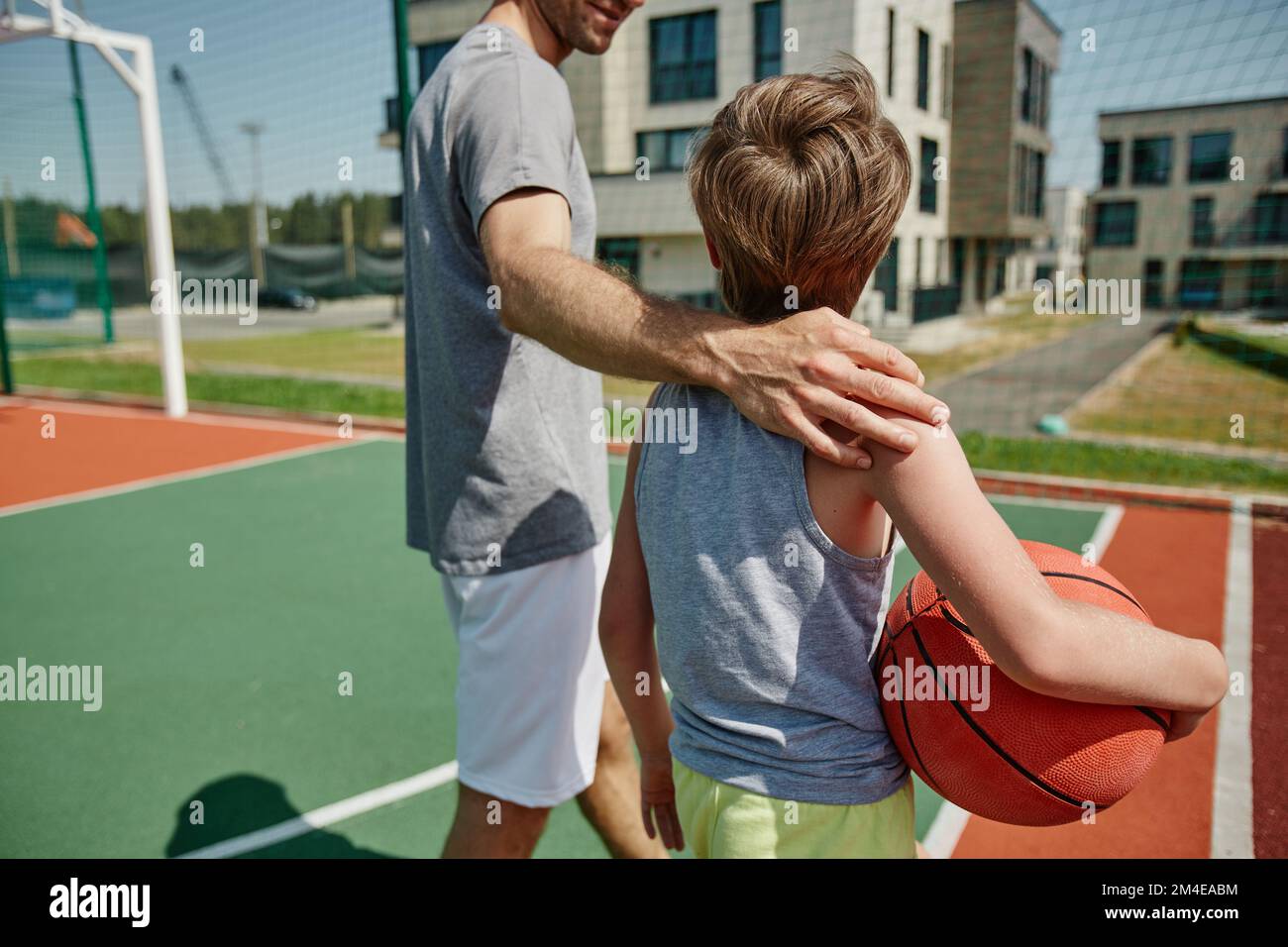 Cerca de padre e hijo felices jugando baloncesto juntos y de pie en la cancha abrazando Foto de stock
