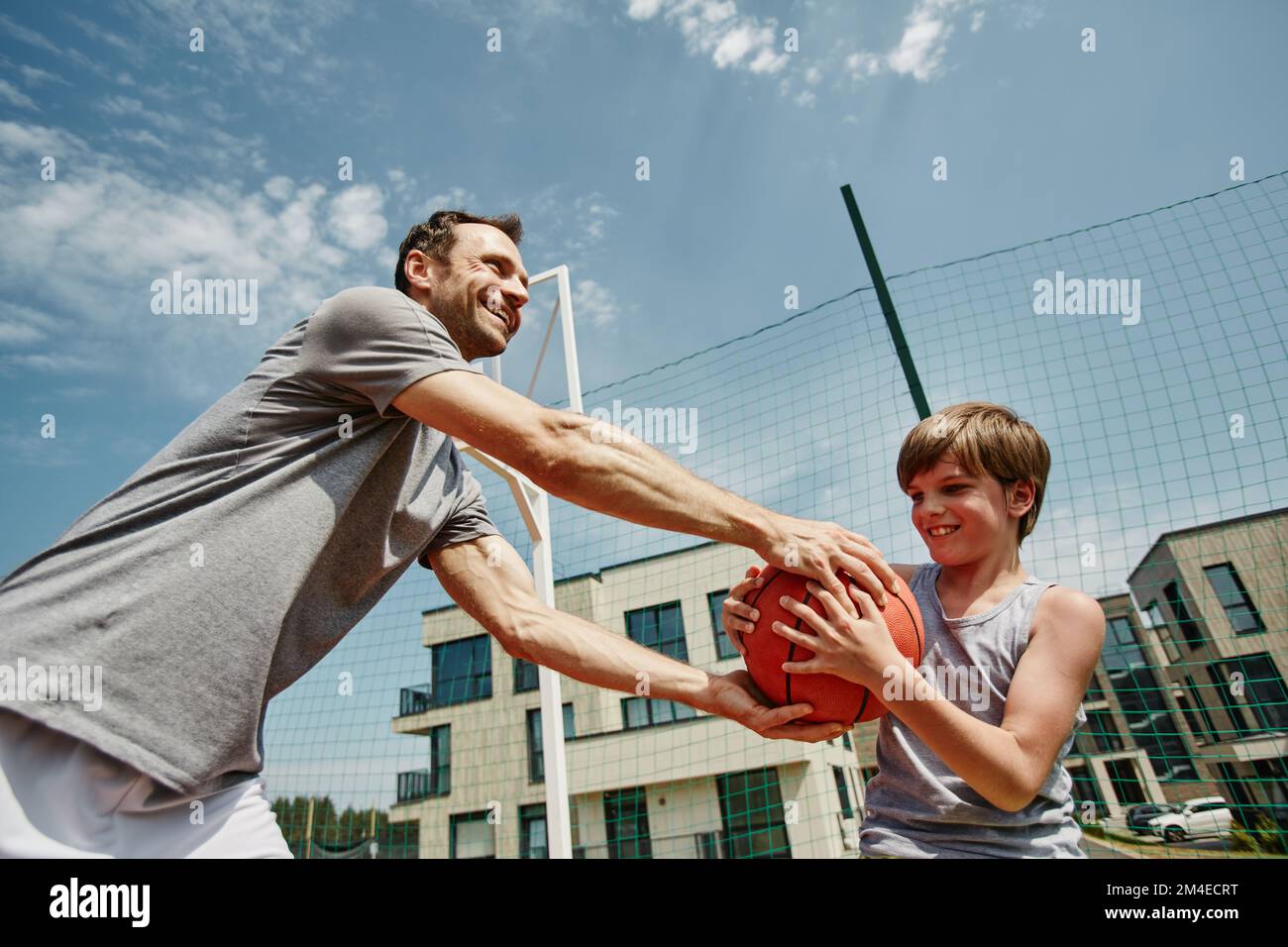 Retrato de ángulo bajo de padre e hijo jugando al baloncesto juntos y sonriendo felizmente contra el cielo Foto de stock