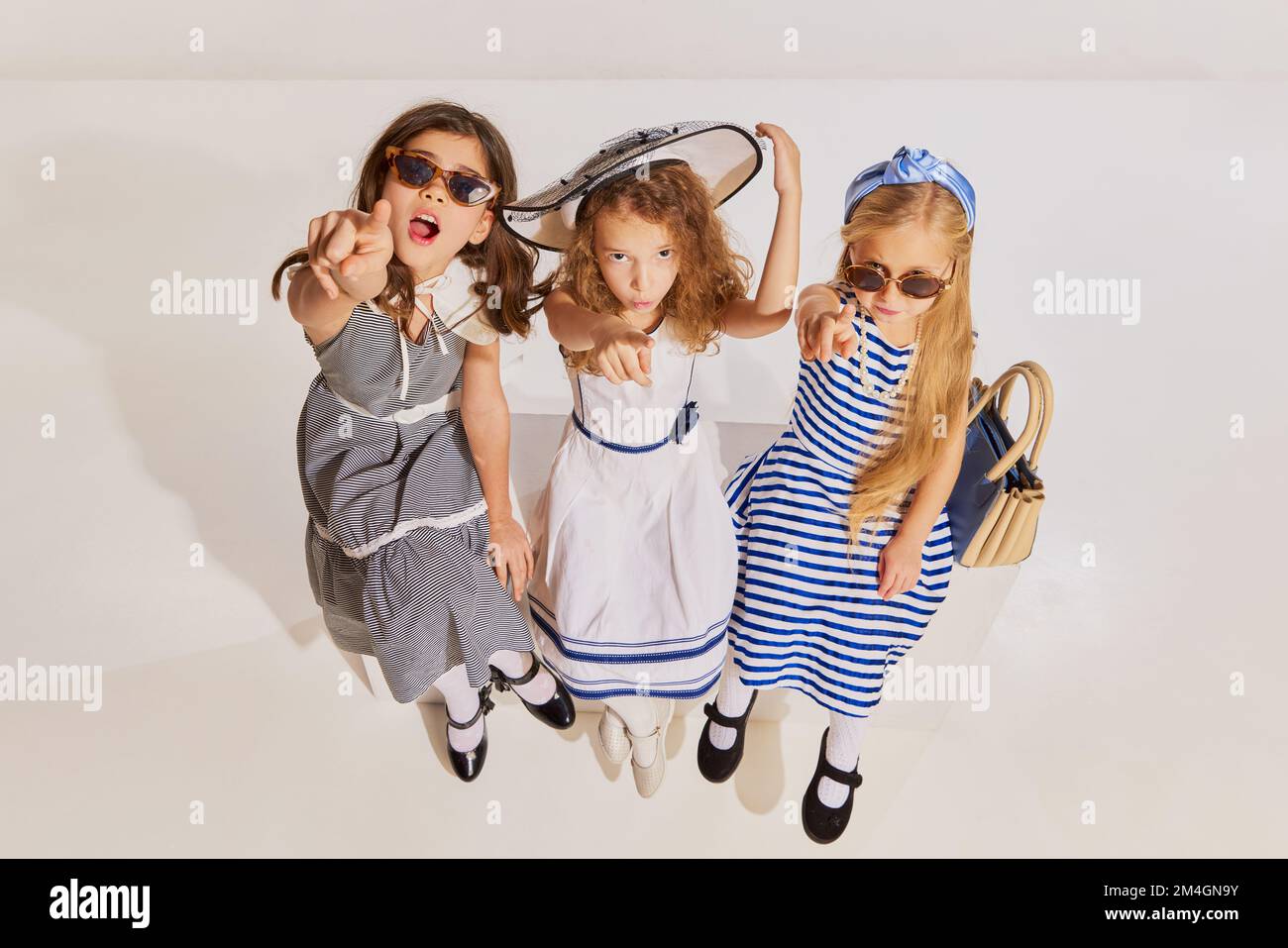 Tres chicas hermosas, niños sentados, posando en vestidos con estilo y gafas de sol sobre fondo gris Fotografía de stock - Alamy Tres chicas hermosas, niños sentados, posando en vestidos con estilo y gafas de sol sobre fondo gris Fotografía de stock - Alamy