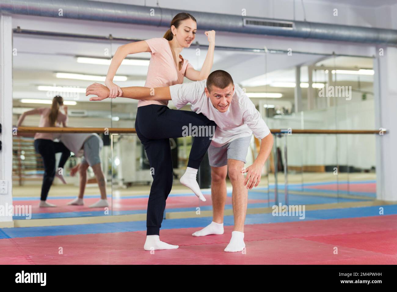 Chica que practica ataques de codo y rodilla con sujeción de brazo a compañero de gorring masculino en el gimnasio Foto de stock