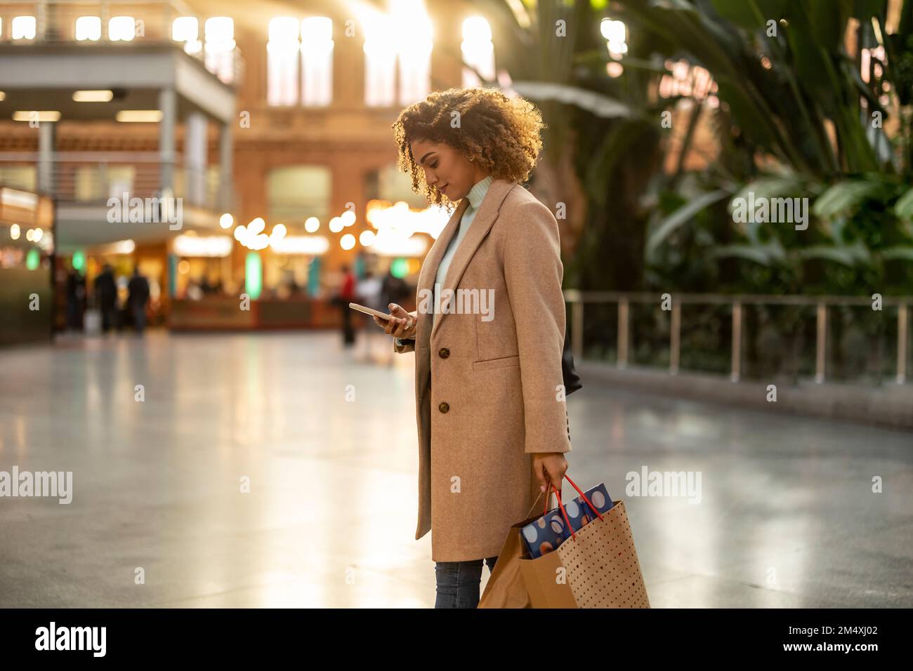 Mujer joven que sostiene los de compras usando teléfono móvil Fotografía stock Alamy
