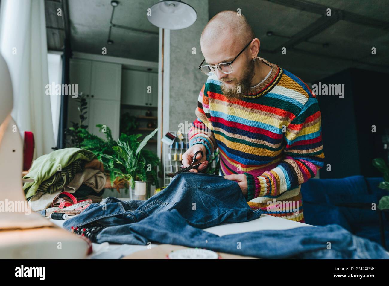 Diseñador de moda que corta la tela vaquera en la mesa en el taller Foto de stock