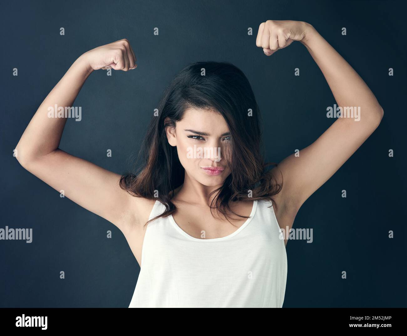 Nunca te disculpes por ser una mujer poderosa. Foto de estudio de una hermosa mujer joven que flexiona sus músculos contra un fondo oscuro. Foto de stock
