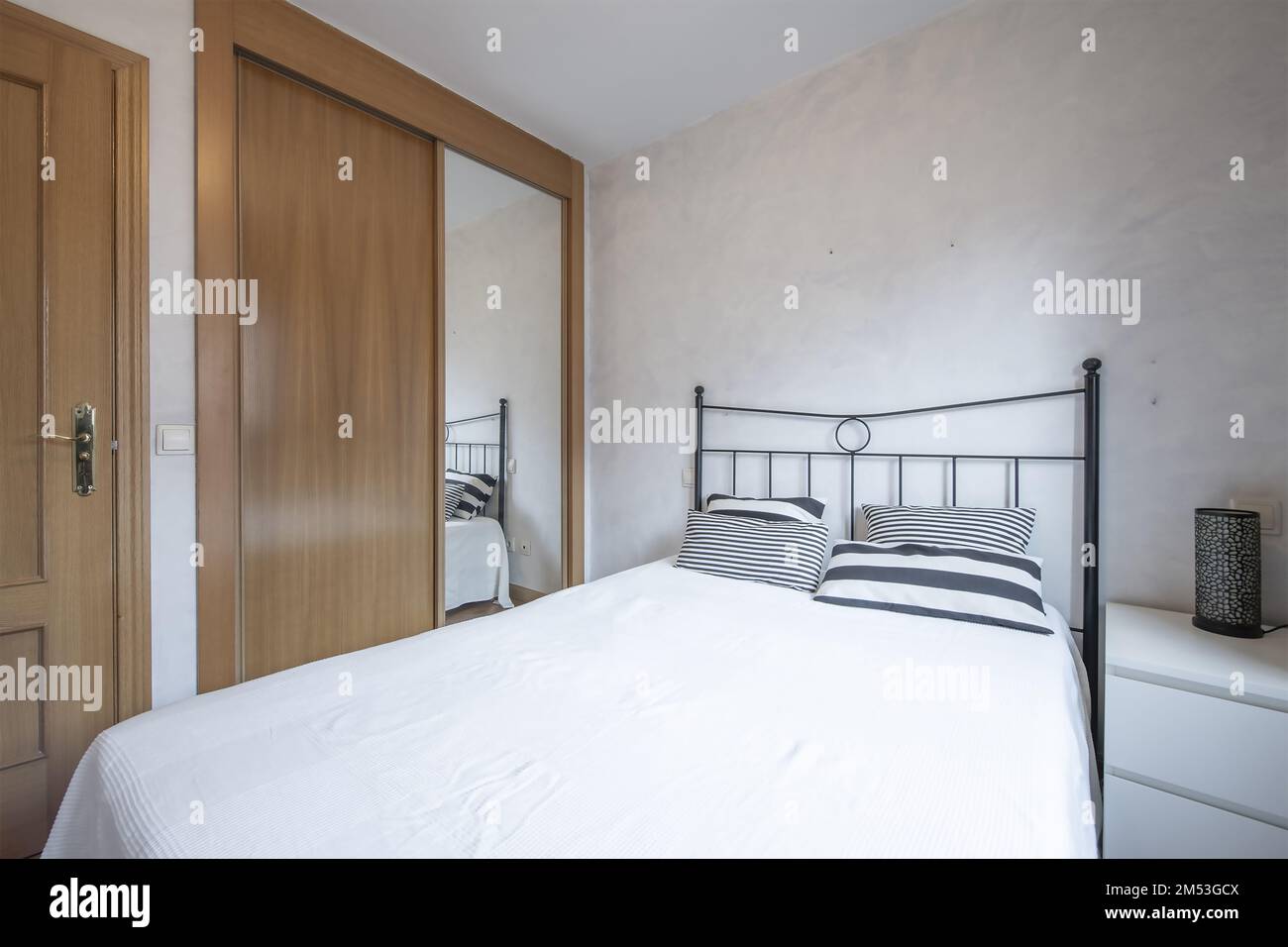 Dormitorio con cama doble con cabecera de metal negro, cómoda blanca y  armario empotrado con espejo y puertas correderas de madera Fotografía de  stock - Alamy