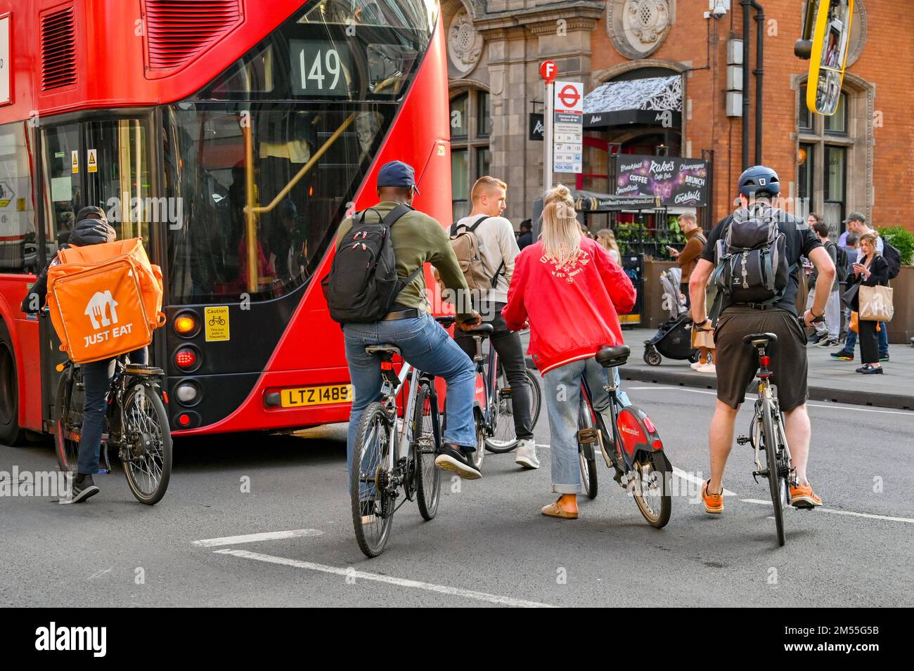 Londres, Inglaterra, Reino Unido - Junio 2022: Ciclistas esperando detrás de un autobús rojo de Londres en una calle en el centro de Londres Foto de stock