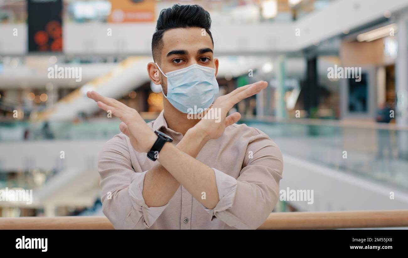 Hombre hispano indio en mascarilla médica muestra gesto prohibido detener las manos cruzadas sin señal de cruce de brazos puesto de empresario enfermo en centro comercial Foto de stock