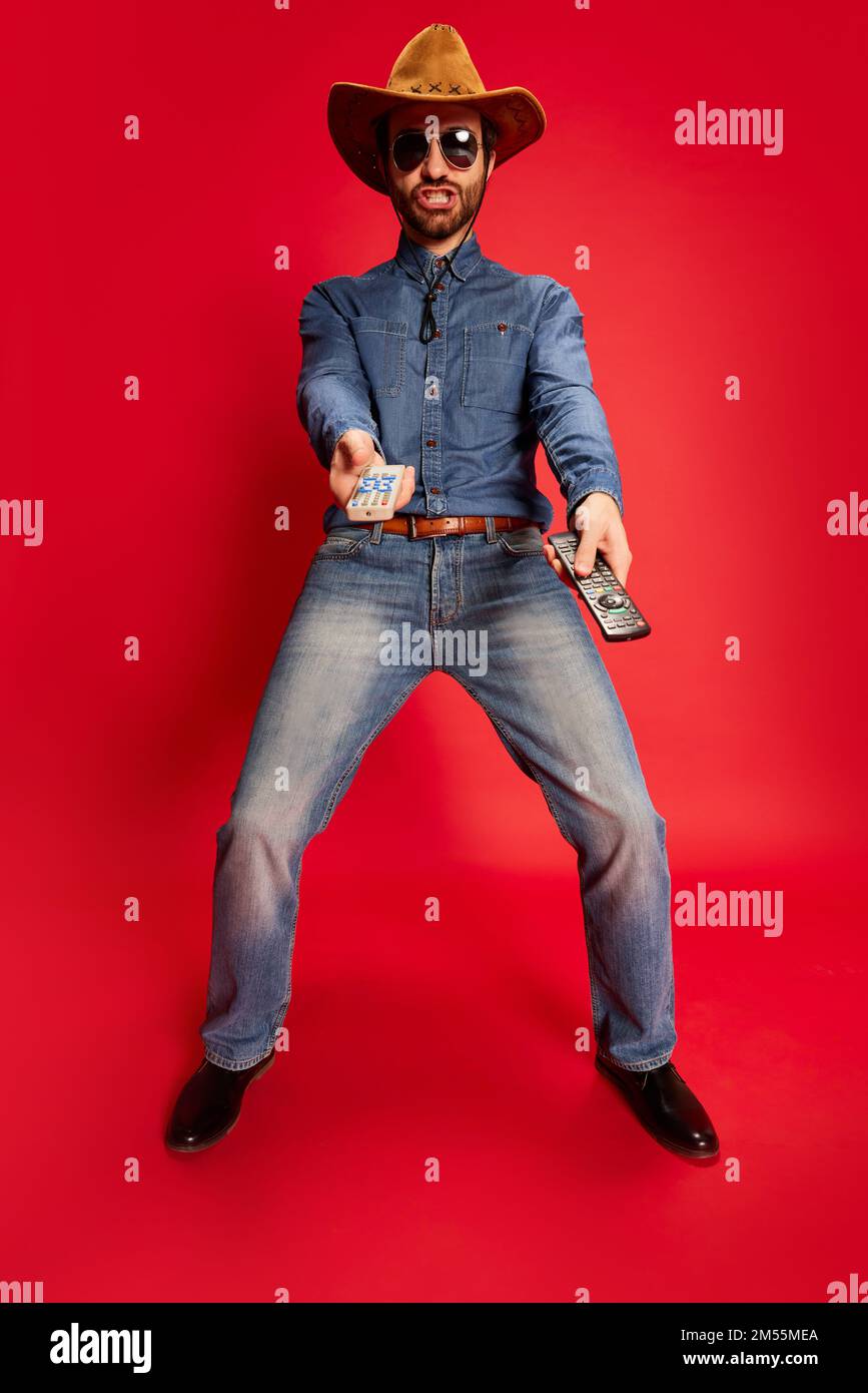 Hombre joven emocionado en traje de estilo vaquero que se divierte, posando  aislado sobre fondo rojo. Modelo en sombrero de vaquero y ropa denim. Moda,  emociones Fotografía de stock - Alamy