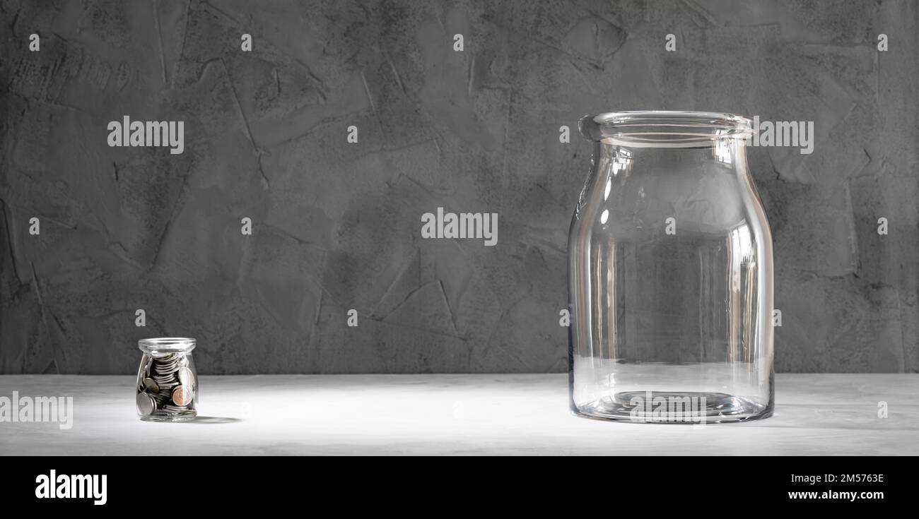 Un pequeño frasco de vidrio con monedas y uno grande vacío. Inicio de un nuevo concepto de negocio Foto de stock