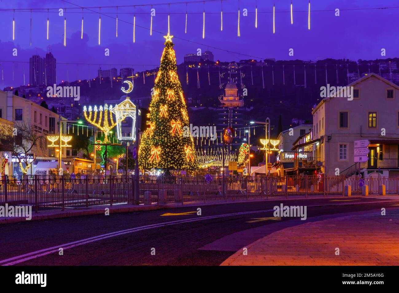 Haifa, Israel - 23 de diciembre de 2022: La escena festiva de las fiestas en la colonia alemana, con un árbol de Navidad, Janucá Menorá, Media Luna Musulmana y Th Foto de stock