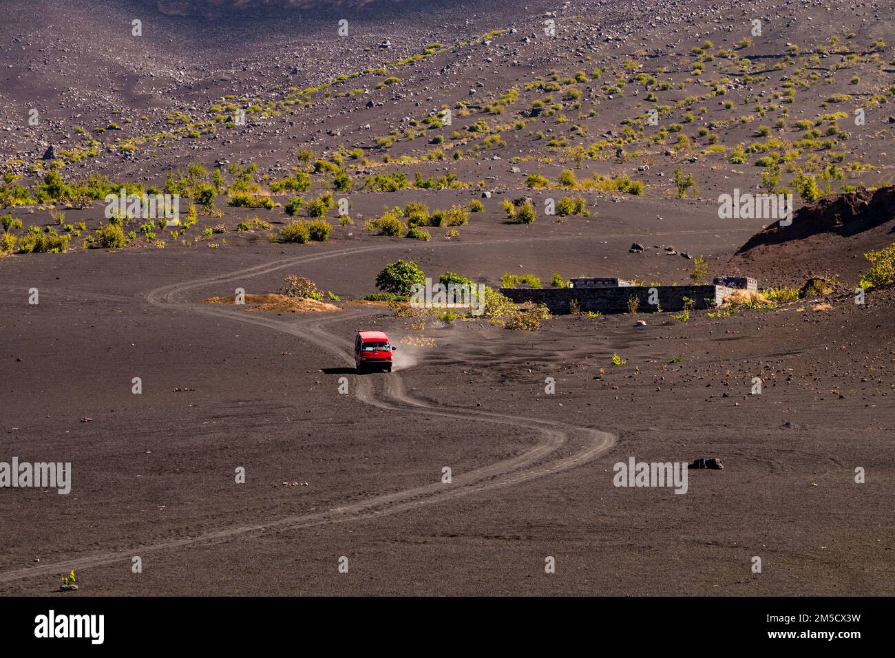 Un minibús rojo conduce a lo largo de un camino de polvo de ceniza en un flanco de Pico do Fogo, Islas de Cabo Verde Foto de stock