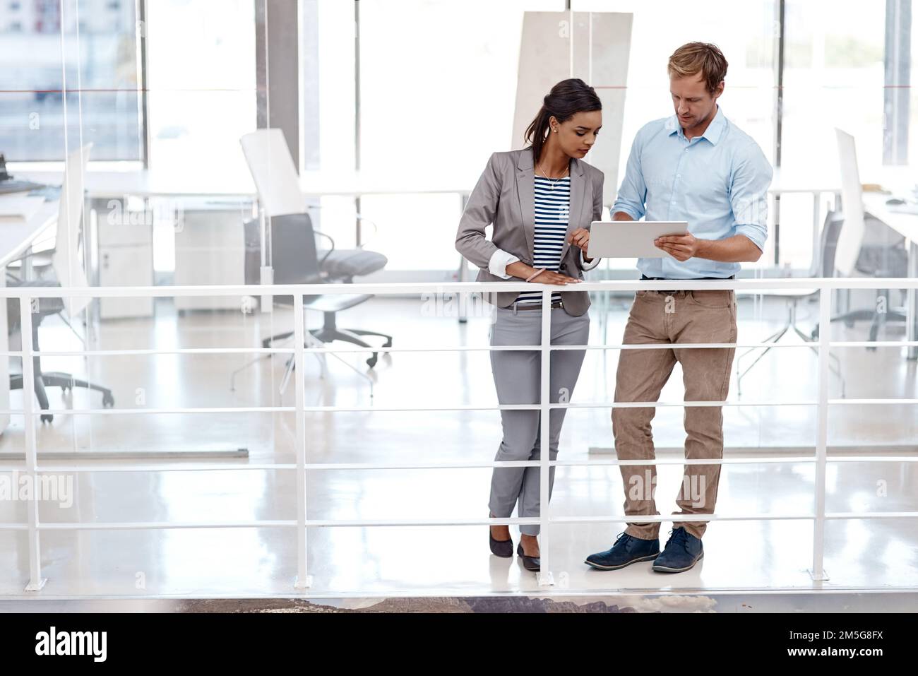 Tal vez tengamos que cambiar nuestro enfoque. Toma completa de dos colegas de buen aspecto de pie en el trabajo discutiendo ideas en una tableta en la oficina. Foto de stock