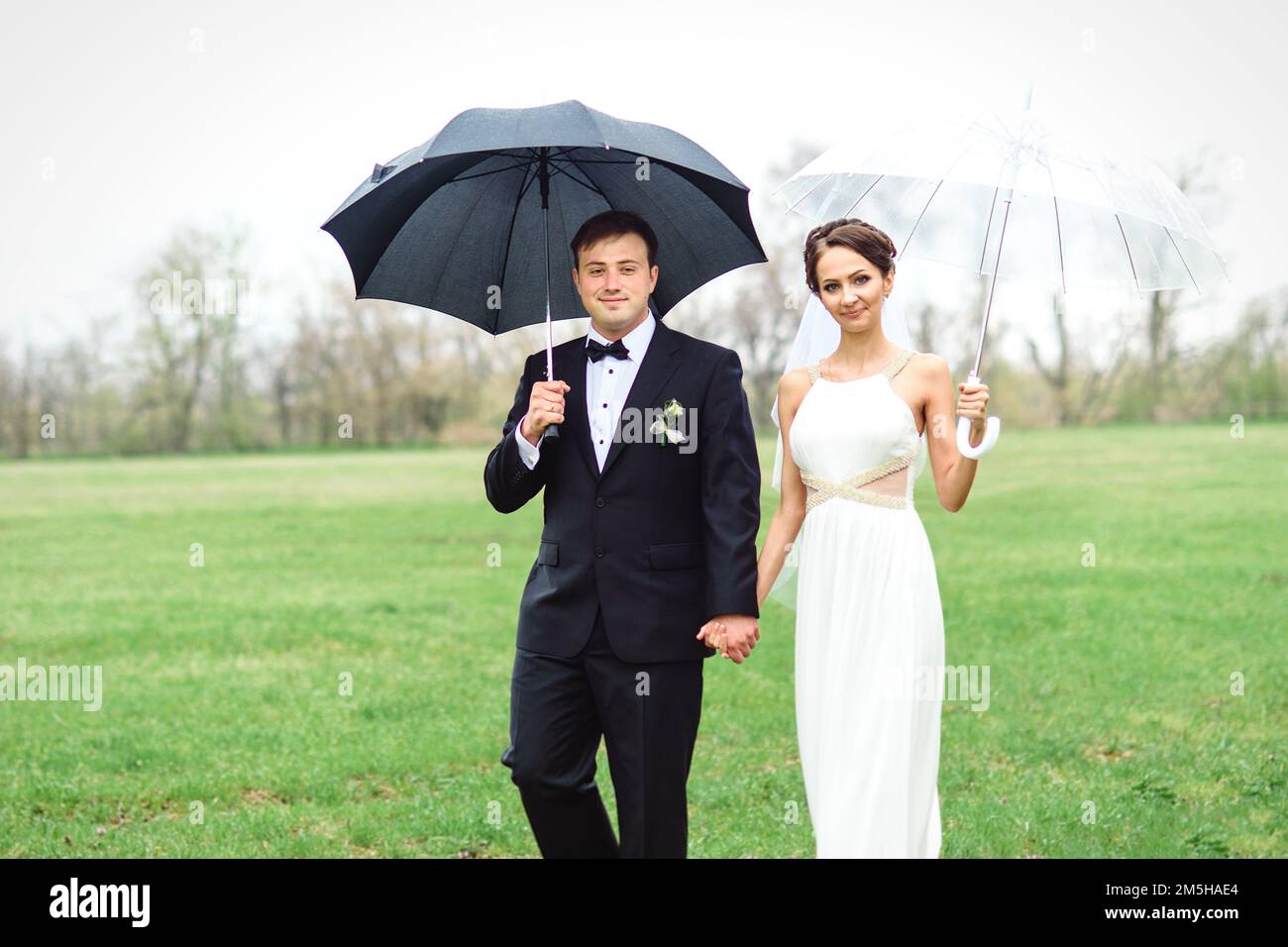 novia y novio en un día lluvioso de boda caminando bajo un paraguas  Fotografía de stock - Alamy