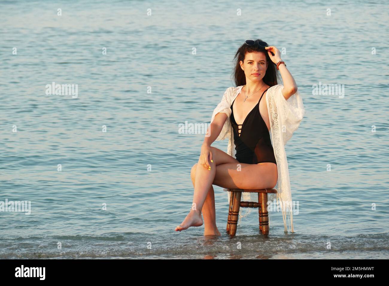 Una mujer hermosa joven posa en la playa del océano. Bastante morena en la playa  blanca túnica y gafas negras sentado en un taburete en el mar Fotografía de  stock - Alamy