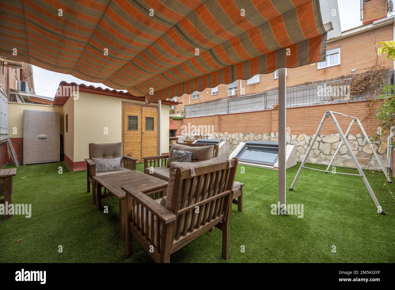 Patio trasero de una casa unifamiliar con toldo gazebo que cubre un conjunto de mesa de teca y sillas en un suelo de césped artificial verde Foto de stock