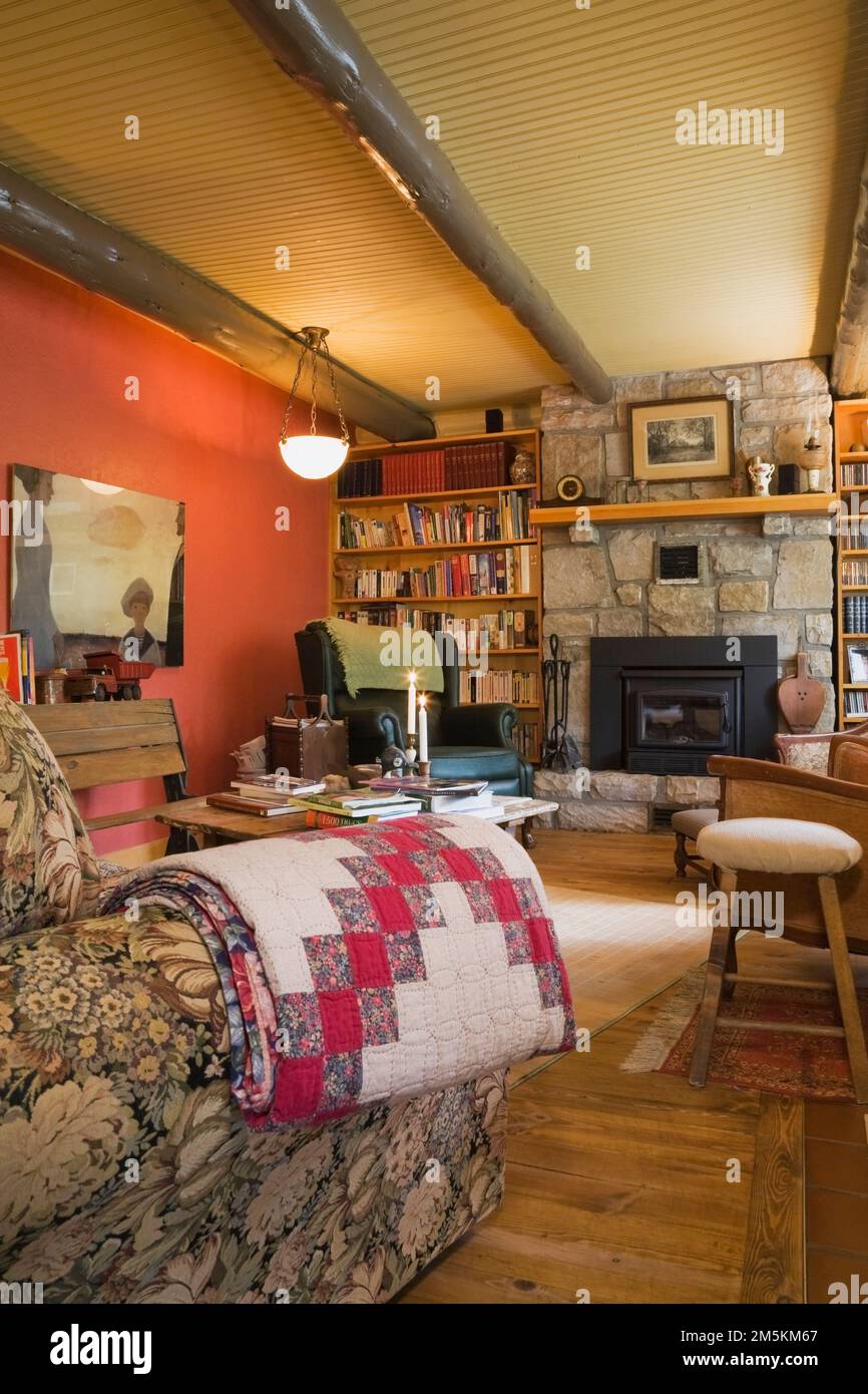Chimenea de piedra cortada bordeada por estanterías y muebles y muebles antiguos en la sala de estar dentro de casa de madera estilo cabaña de campo. Foto de stock