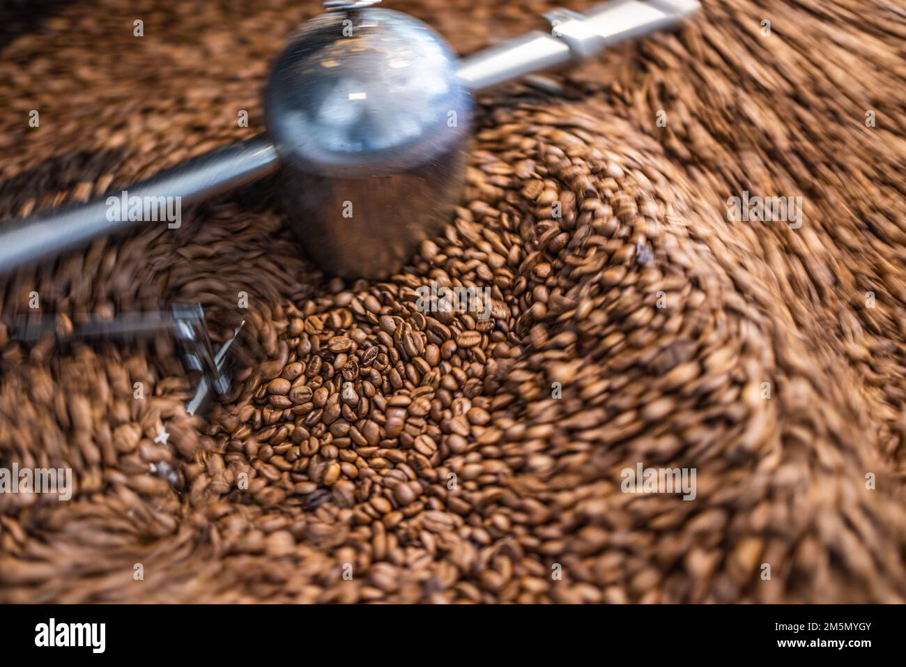 Mejor fondo de café. Granos de café recién tostados en movimiento. Concepto de primer plano de bebida caliente artística. Tostador de café cilindro para asar y mezclar Foto de stock