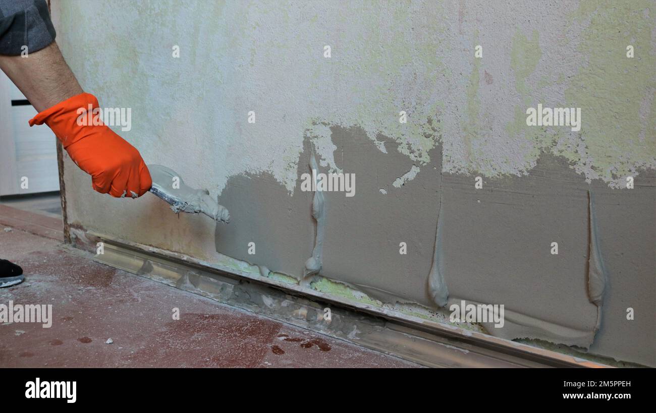 mortero de plástico aplicado en una pared de la habitación en capas gruesas para nivelar la superficie, el yeso aplica el mortero en la textura de la pared con una espátula Foto de stock
