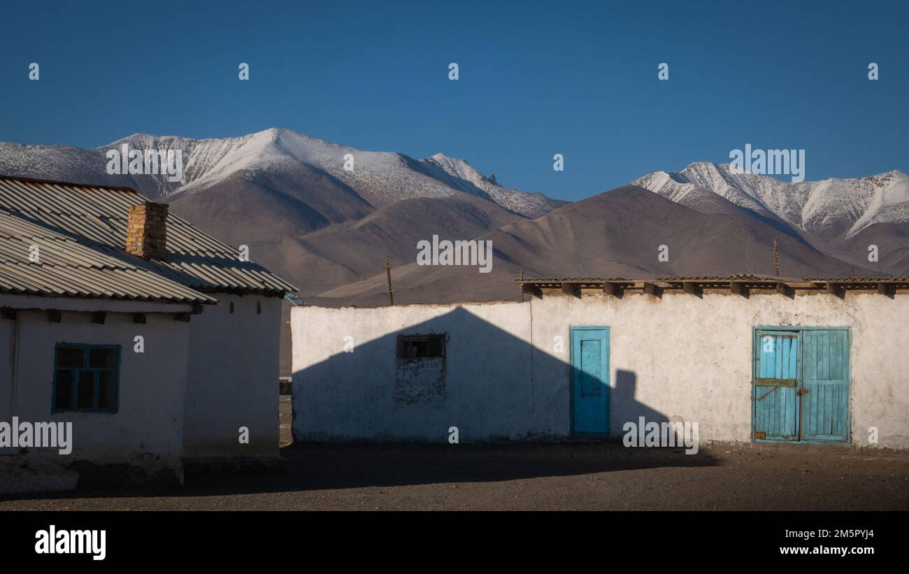 Vista escénica del paisaje de las casas de pueblo de Karakul con fondo de montaña nevada, distrito de Murghab, Gorno-Badakshan, Pamir de Tayikistán Foto de stock