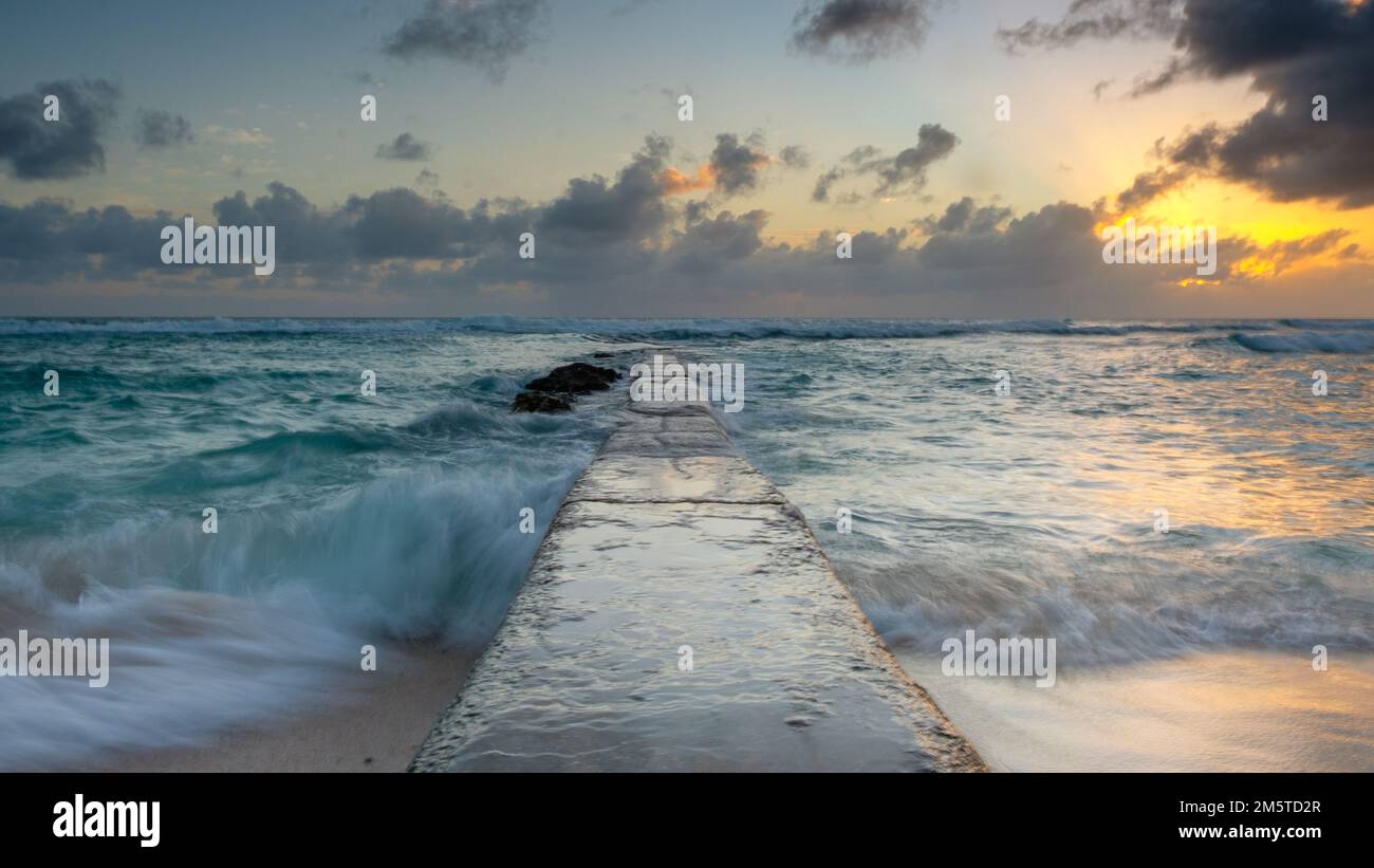 Barbados - una vista en perspectiva de un muelle de piedra con una puesta de sol colorida Foto de stock