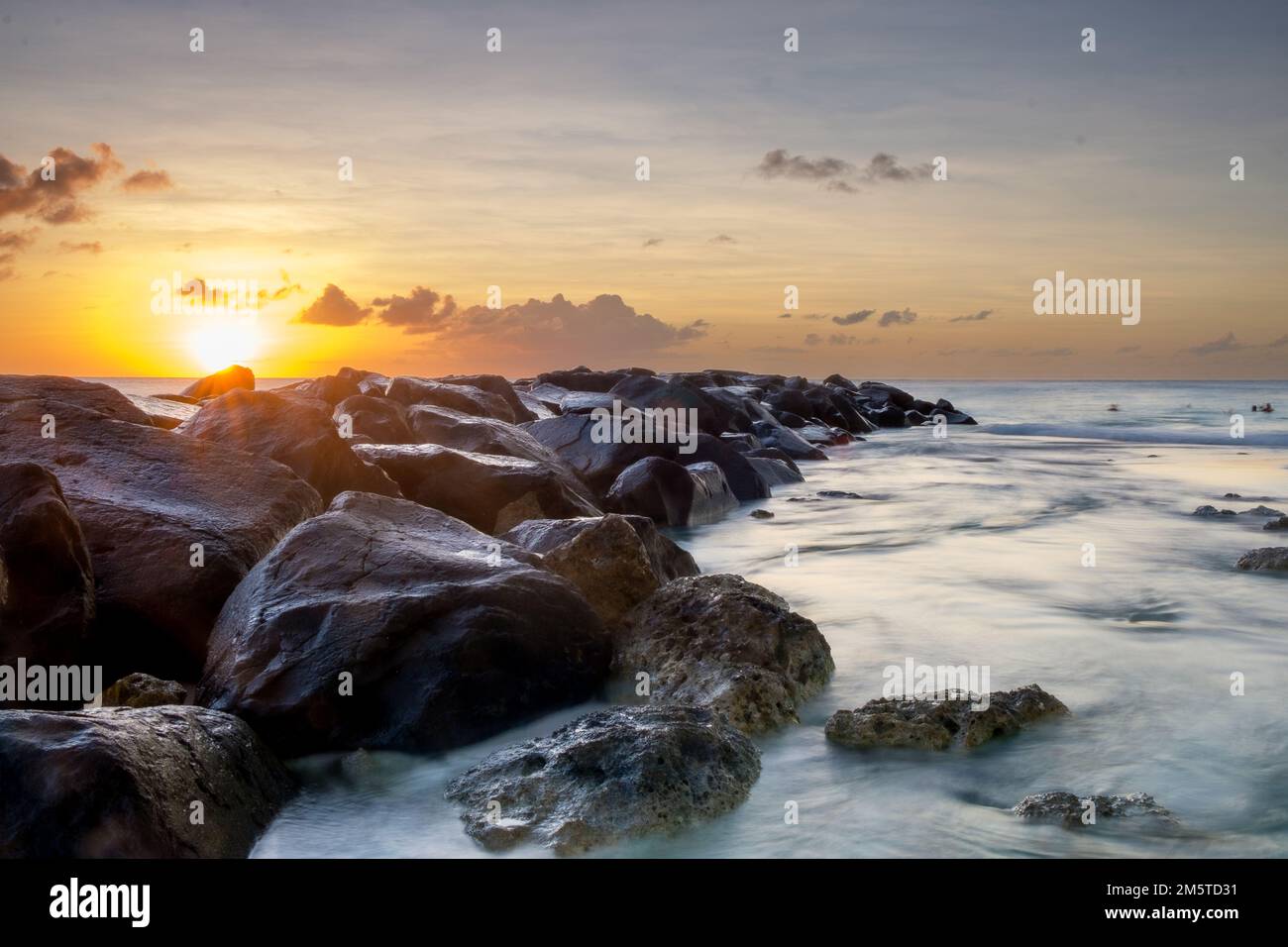 Puesta de sol tranquila con grandes piedras entrando en el mar Foto de stock