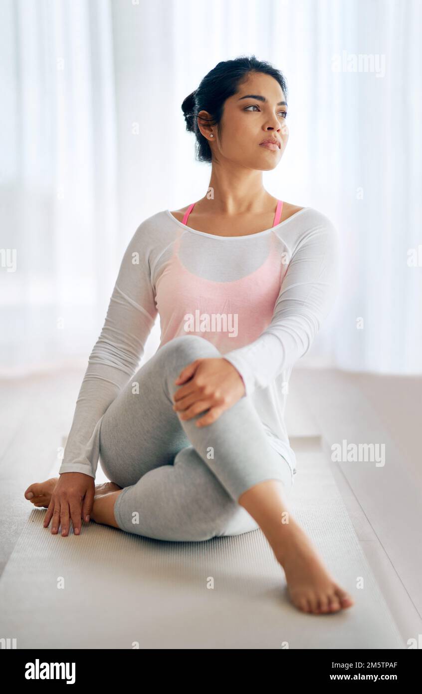 Encontrando su centro espiritual. una mujer joven estirándose durante su rutina de yoga. Foto de stock