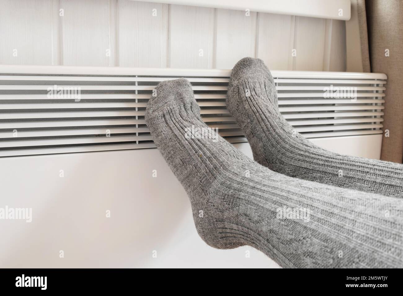 Piernas en calcetines de punto calentando sobre calentador eléctrico. Mujer  congelada que lleva unos calcetines de lana calientes que se congelan para  el frío del invierno. Incomodidad pasar tiempo en hom Fotografía