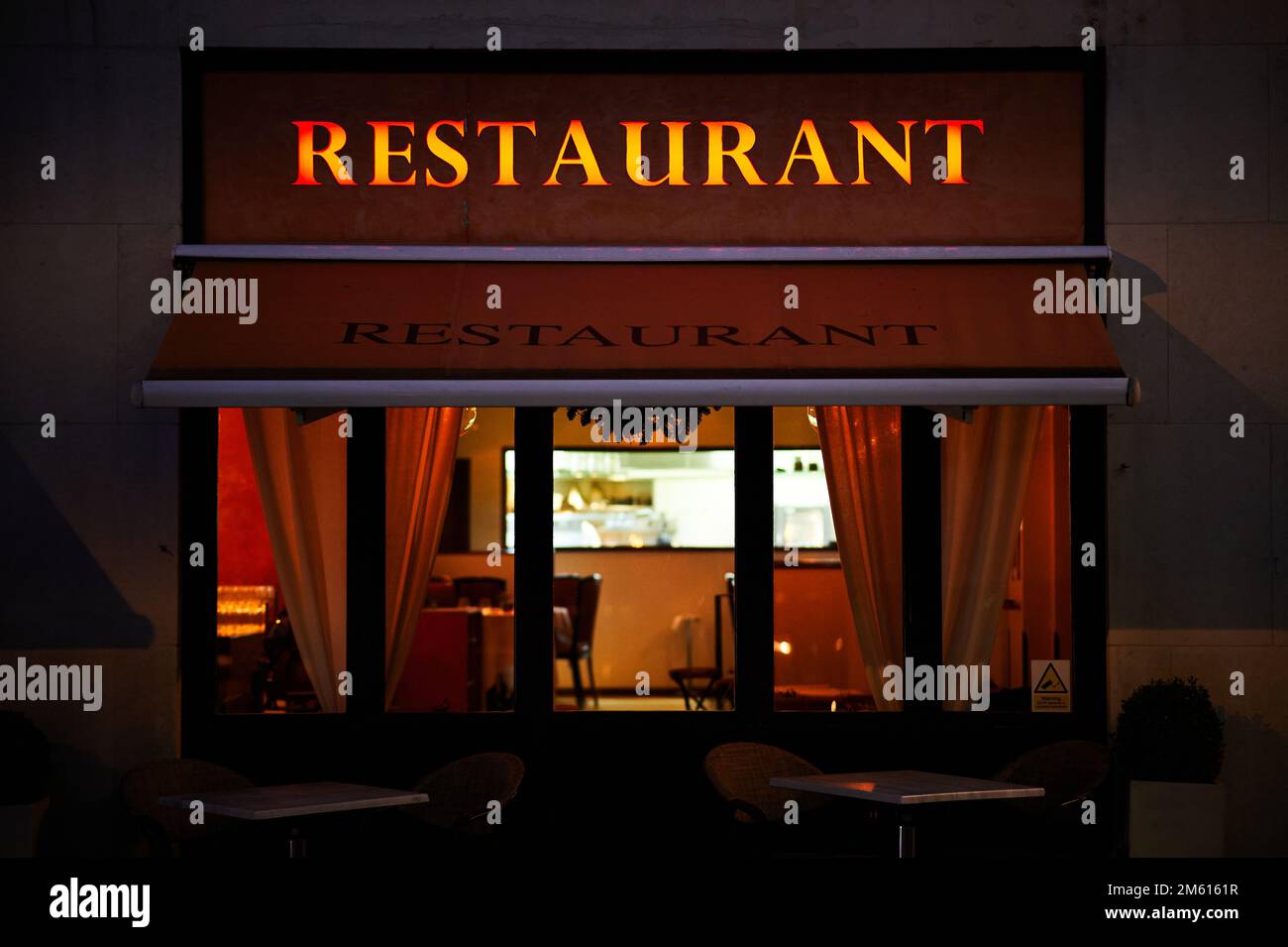 23 dic 2022 - Londres Reino Unido: Letrero iluminado del restaurante por la noche sobre el restaurante con mesa exterior y asientos Foto de stock