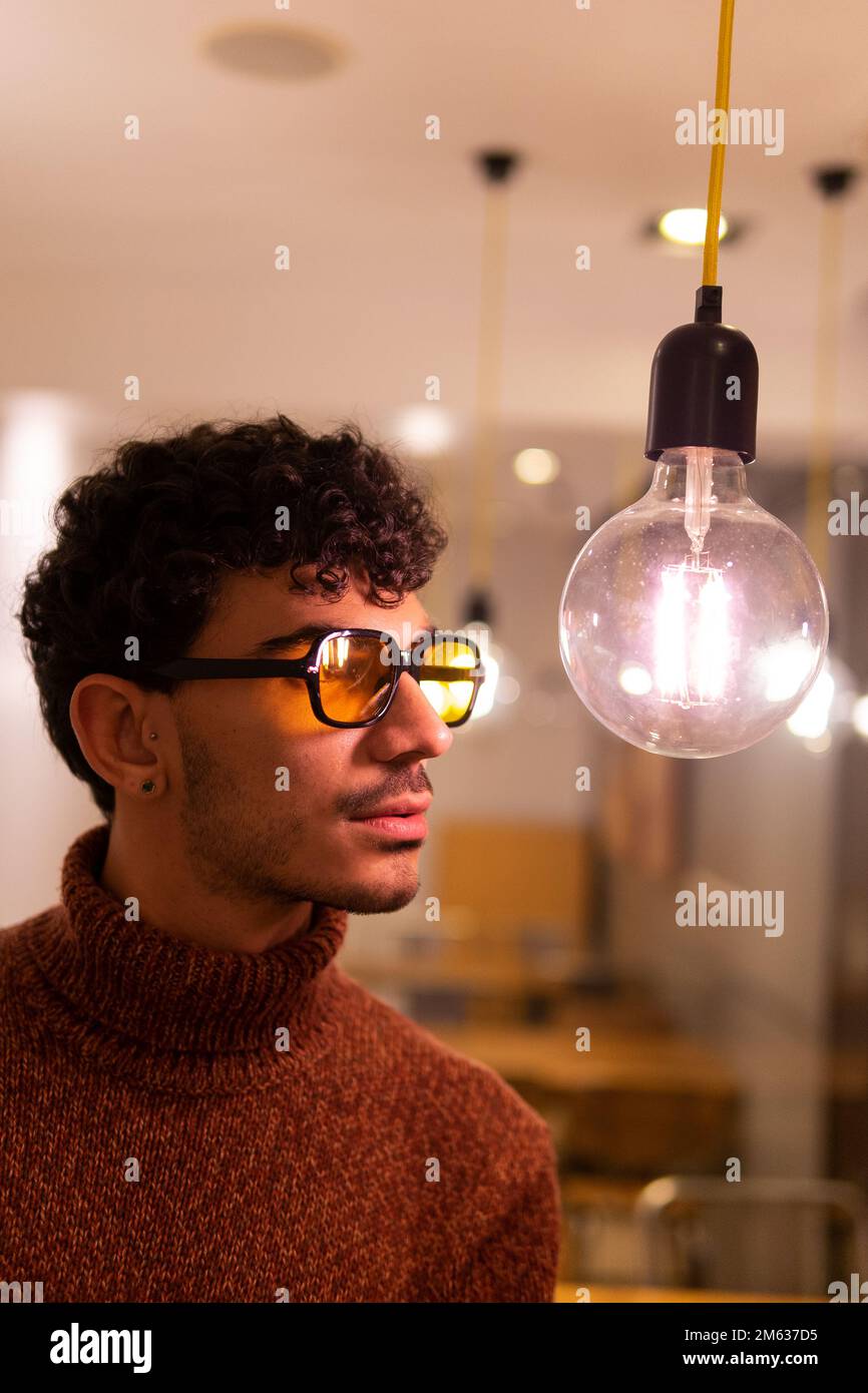 Hombre joven en suéter caliente y gafas de sol de pie cerca de la bombilla de cristal transparente en café Fotografía de stock - Alamy