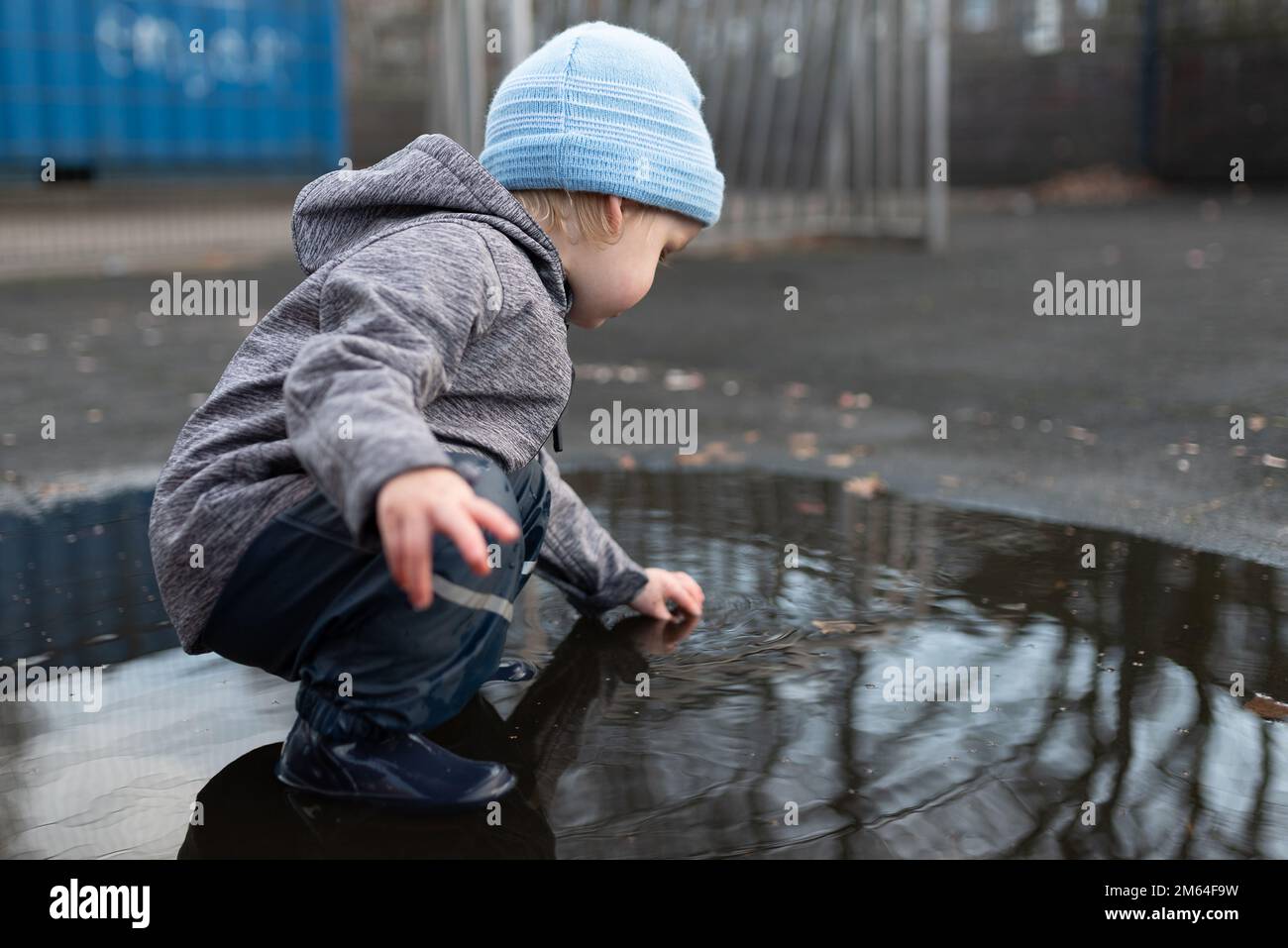 niño de dos años en pantalones de lluvia y botas de goma jugando en charco de agua después de la ducha de lluvia Foto de stock