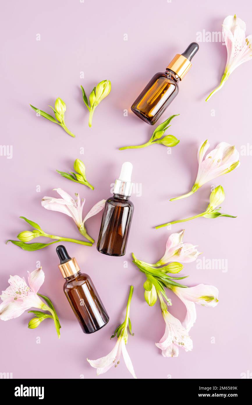 tres botellas con un cuentagotas de vidrio ámbar con un cosmético para el  cuidado de la piel de la cara y el cuerpo sobre un fondo púrpura con brotes  de flores de