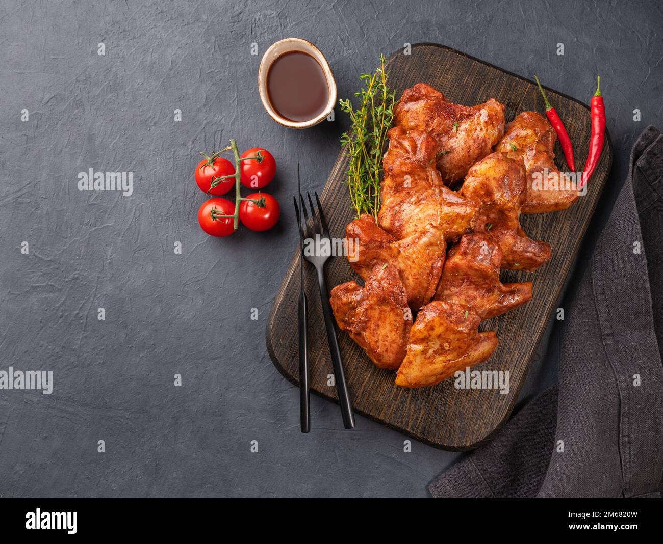 Alitas de pollo bbq con salsa, tomate y hierba fresca en una tabla de  madera sobre un fondo oscuro. El concepto de snacks para una fiesta. Vista  superior y espacio de copia