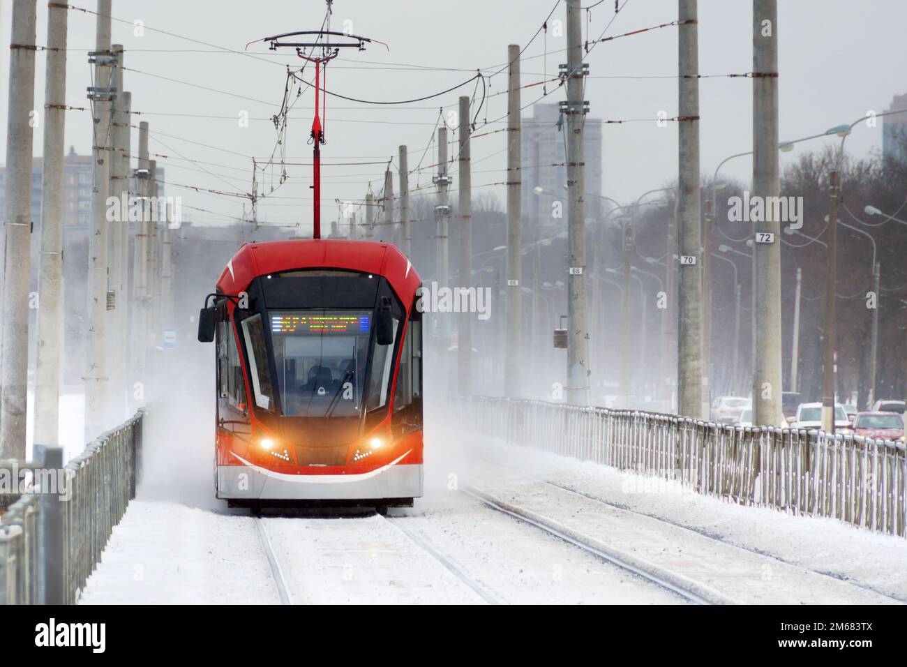 El tranvía rojo corre durante una tormenta de nieve de invierno en la ciudad Foto de stock