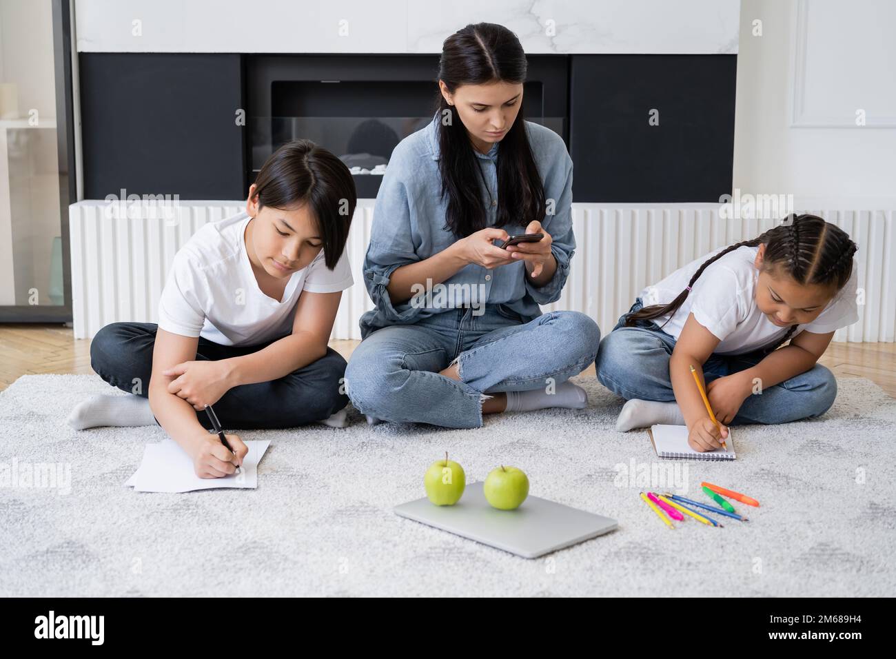 Madre ocupada usando smartphone mientras que los niños asiáticos dibujan y se sientan en el piso en casa, imagen de stock Foto de stock