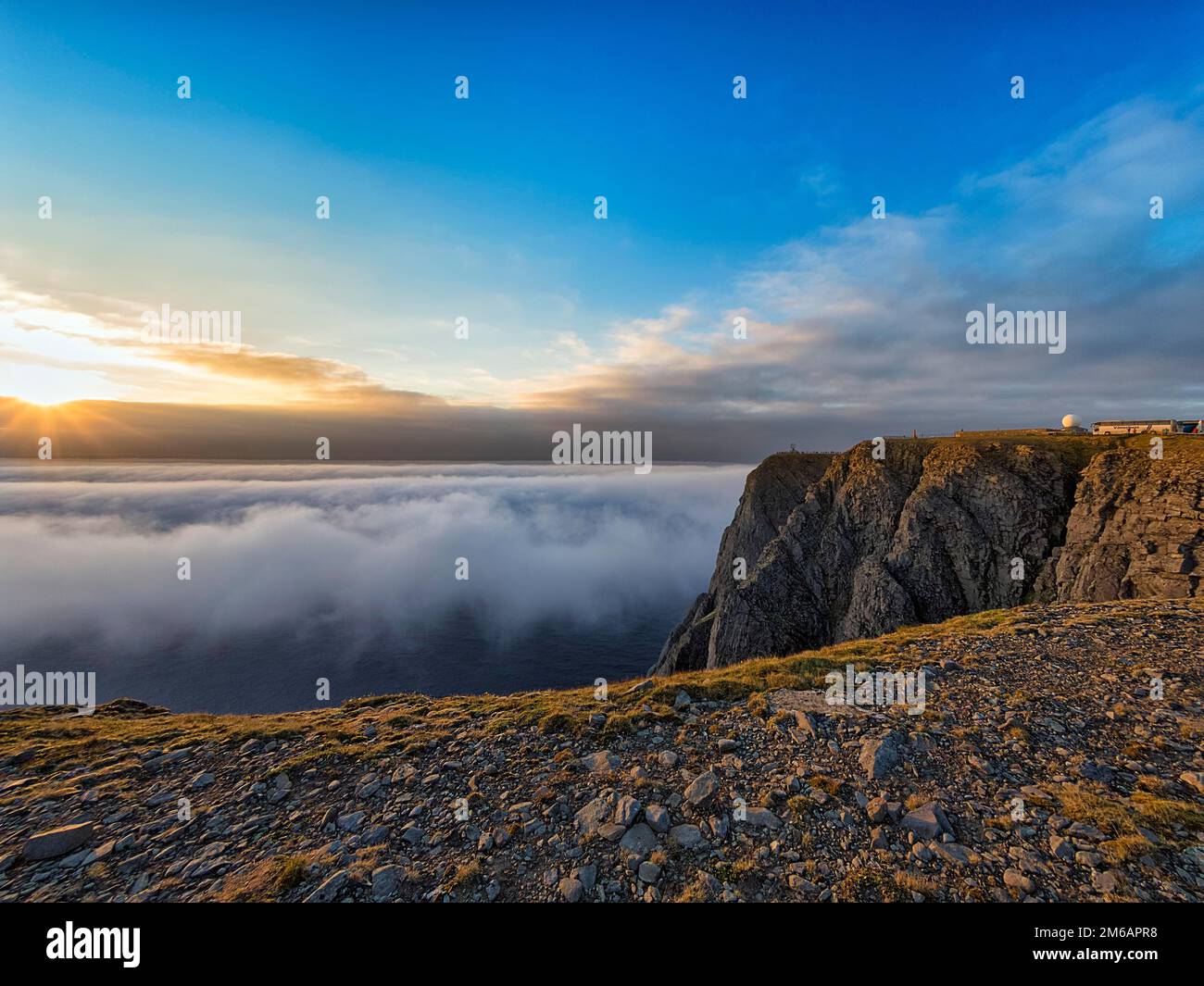 Costa de esquisto rocoso, mar de nubes con sol de medianoche, plataforma de visitantes en el horizonte, Cabo Norte, Nordkapp, Mageroya, Finnmark, Océano Ártico, Noruega Foto de stock
