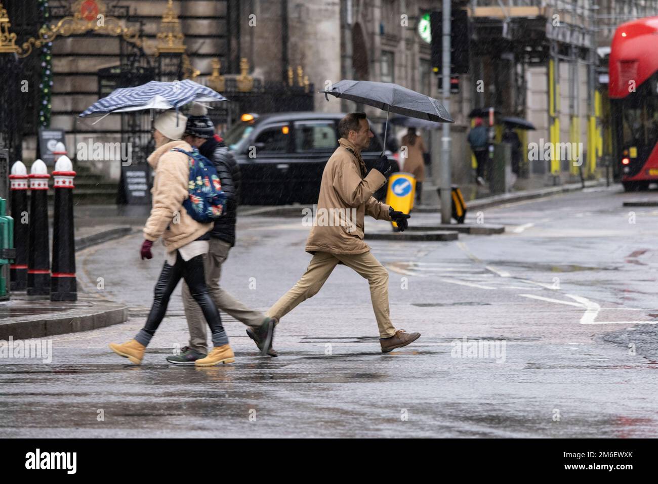 La gente se cubre de la lluvia de invierno bajo sus paraguas fuera del Banco de Inglaterra, en la Milla Cuadrada, Ciudad de Londres, Reino Unido Foto de stock