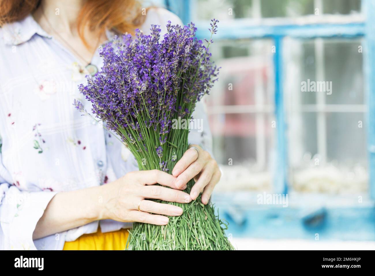 chica sosteniendo un ramo de lavanda contra el fondo de la ventana de la casa vieja Foto de stock